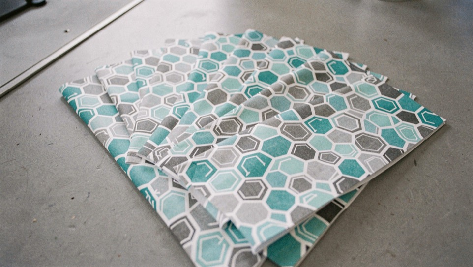 Arrow wrap sheets printed with repeating hexagon patterns in gray, turquoise and white, fanned out on a neutral gray work surface